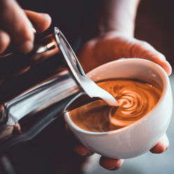 Midsection of person pouring milk in coffee cup