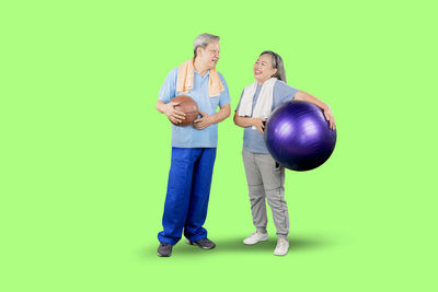 Couple holding ball while standing against green background