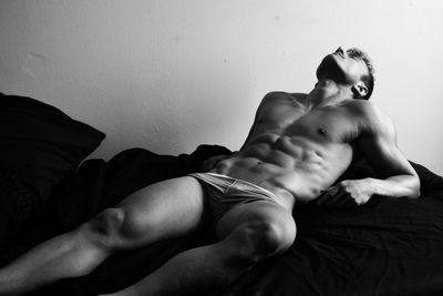 Low section of naked male  lying on bed at home with muscles model athlete