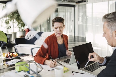 Businesswoman writing while having discussion with colleague