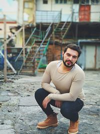 Portrait of young man crouching on walkway