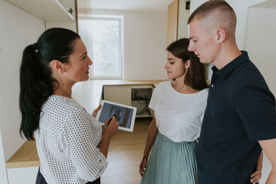 Woman explaining blueprint to couple on tablet at home