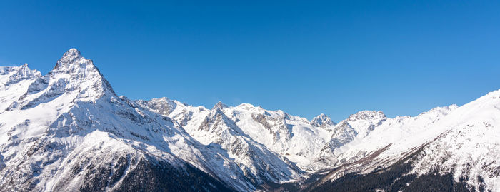 Panoramic view of winter snowy mountains in caucasus region in russia with blue sky