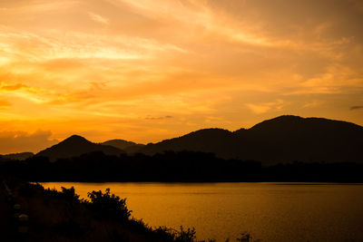 Scenic view of lake by silhouette mountains against orange sky