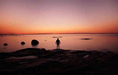 Silhouette man standing on rock by sea against sky during sunset