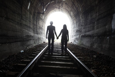 Rear view of silhouette people walking on railroad tracks