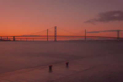 Suspension bridge over sea against sky during sunset