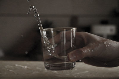 Close-up of hand splashing water in glass