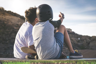 Rear view of boy sitting with friend on retaining wall