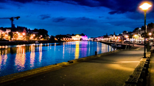 Illuminated city by river against sky at night