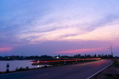 Road by city against sky at sunset