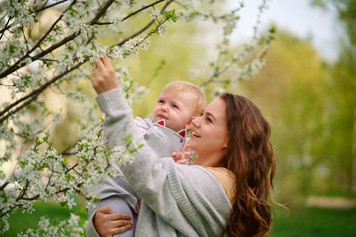 Mother holding a baby in her arms in a blooming cherry garden