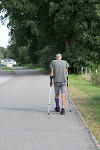 A man with a broken leg is walking down the street, on his left leg he has special boot for walking