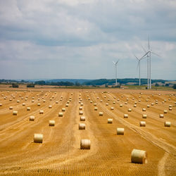 Hay bales and wind turbines on agriculture landscape against cloudy sky