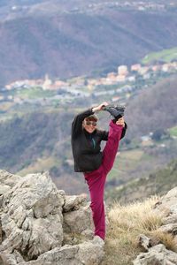 Full length of woman stretching leg on mountain