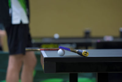 Close-up of table tennis racket and ball on table with person in background