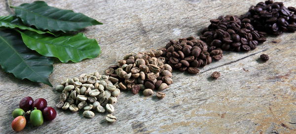 Close-up of various roasted coffee beans with leaves on table