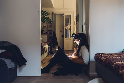 Woman with virtual reality headset sitting by wall at home