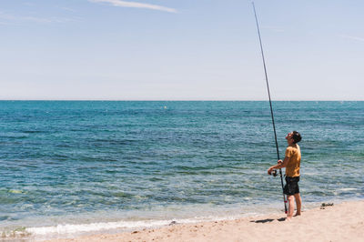 Full length of man fishing on sea against sky