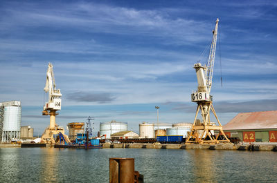 Cranes at commercial dock against sky