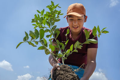 Low angle view of woman holding plant against sky