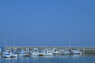 Sailboats moored on sea against clear blue sky