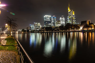Illuminated buildings by river against sky at night