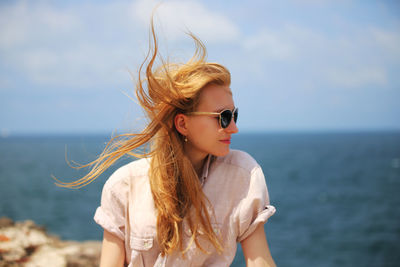 Beautiful young woman wearing sunglasses against sea