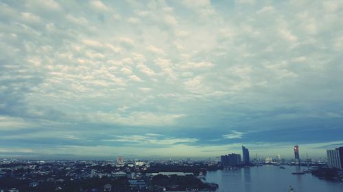 City at waterfront against cloudy sky