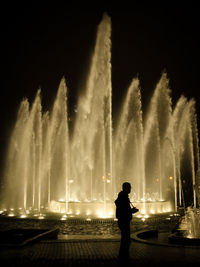 Silhouette woman standing by fountain against sky at night