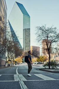Man standing on road by modern buildings in city against sky
