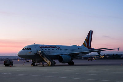 Airplane flying over airport runway against sky during sunset