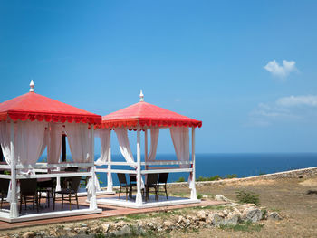 Table and chairs arranged in built structure by sea against blue sky