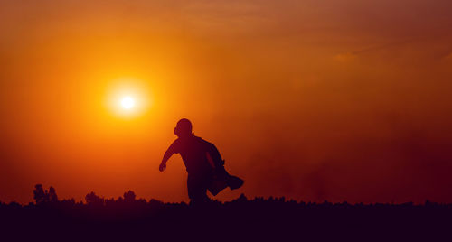 Silhouette man standing on field against orange sky