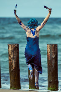 Young woman performance artist in dark blue dress smeared with blue gouache paints happily dancing