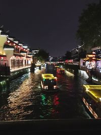 Illuminated city by river against sky at night