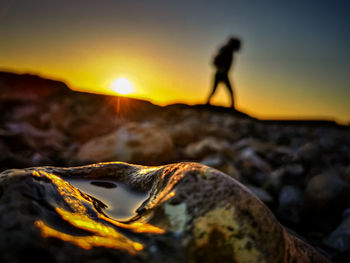 Silhouette man standing on rock against sky during sunset