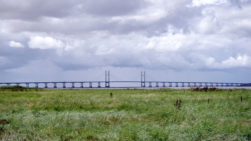 View of suspension bridge in field against cloudy sky
