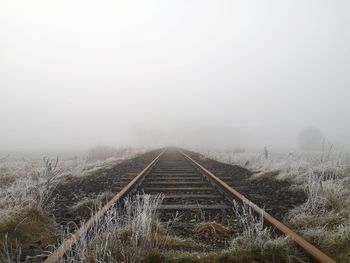 Railroad tracks on field against sky during winter