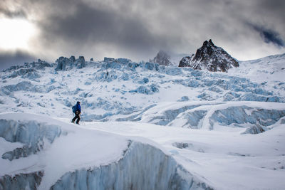 Person hiking on snow covered mountain against cloudy sky