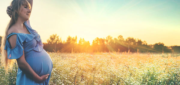 Young woman standing on field against sky during sunset