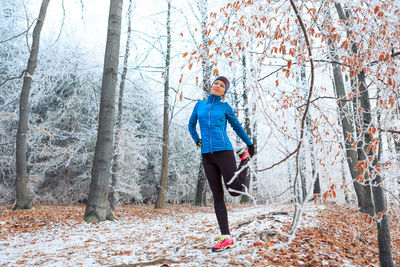 Full length of woman stretching in forest during winter