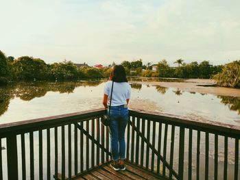 Rear view of woman standing by railing against lake