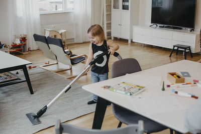 Smiling girl vacuum cleaning living room