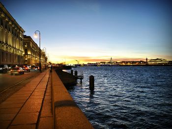 City street by sea against sky at sunset