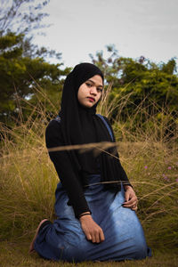 Young woman looking away while sitting on field