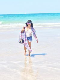 Full length of young woman standing on beach against clear sky