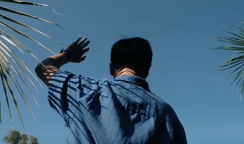 Rear view of man standing against blue sky