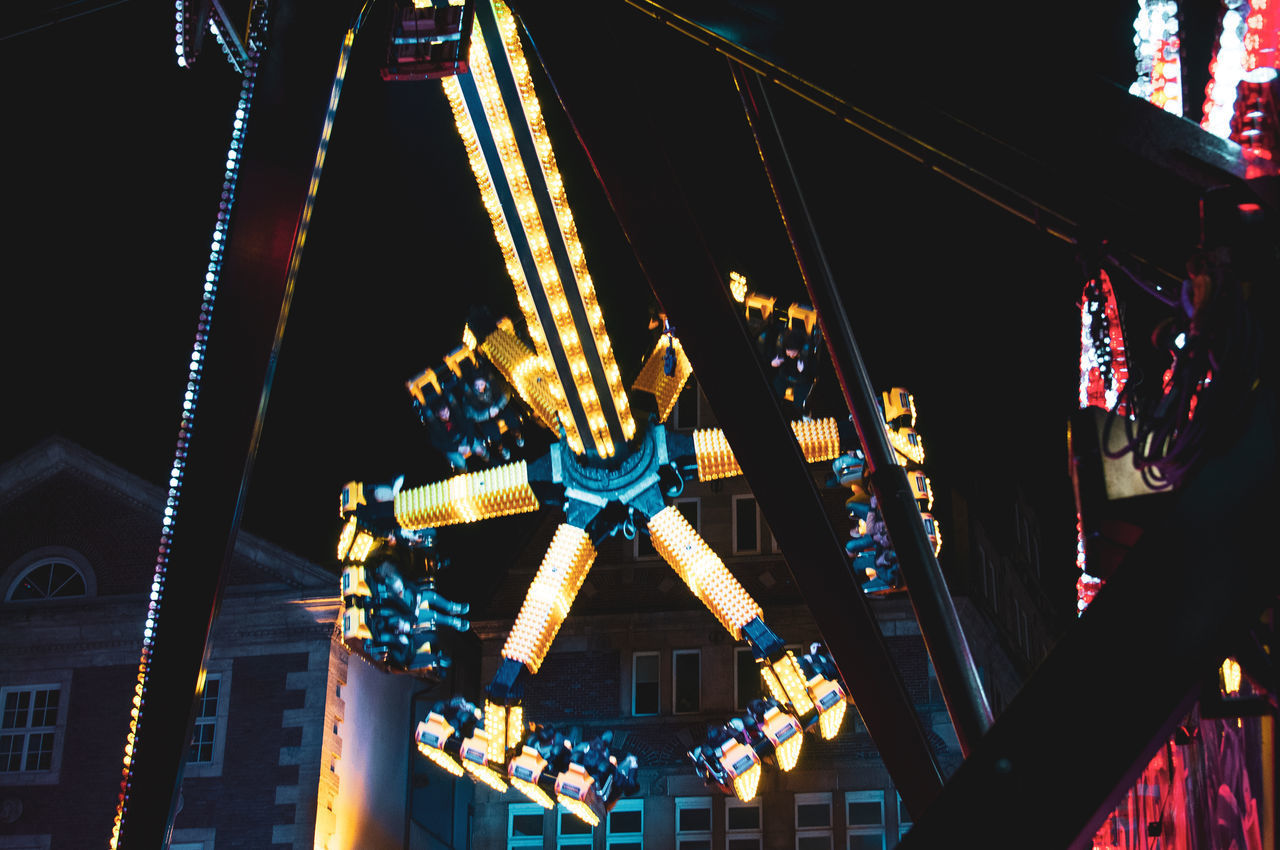 LOW ANGLE VIEW OF ILLUMINATED FERRIS WHEEL AGAINST BUILDINGS