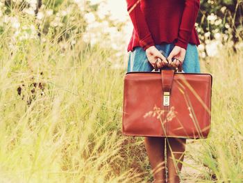 Low section of woman with leather bag standing on grassy field